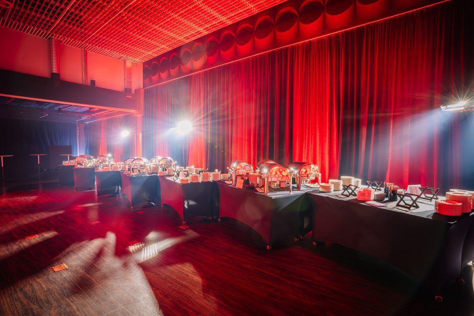 A banquet hall set for dinner under red stage lighting