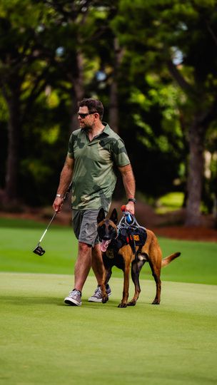 A golfer walking a service dog across the green