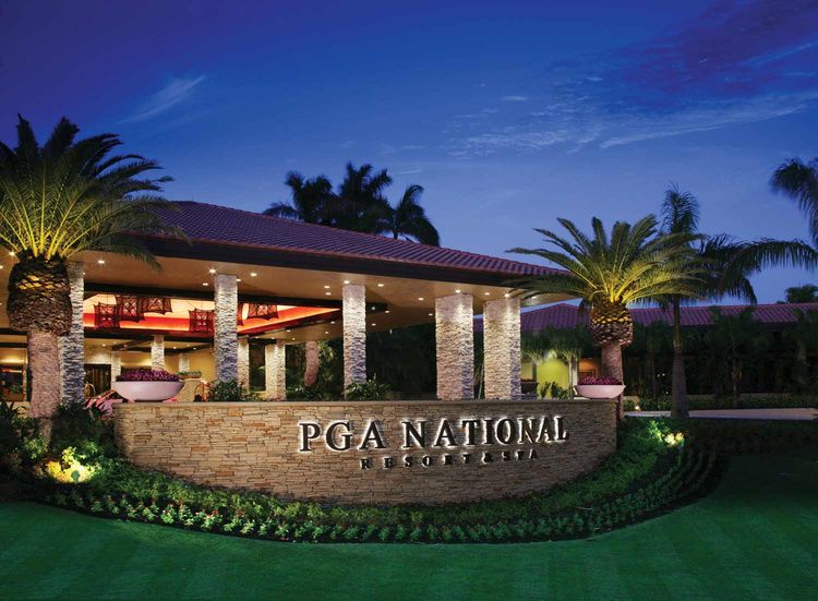 The entrance to PGA National Resort at dusk, lit palms and the stone sign