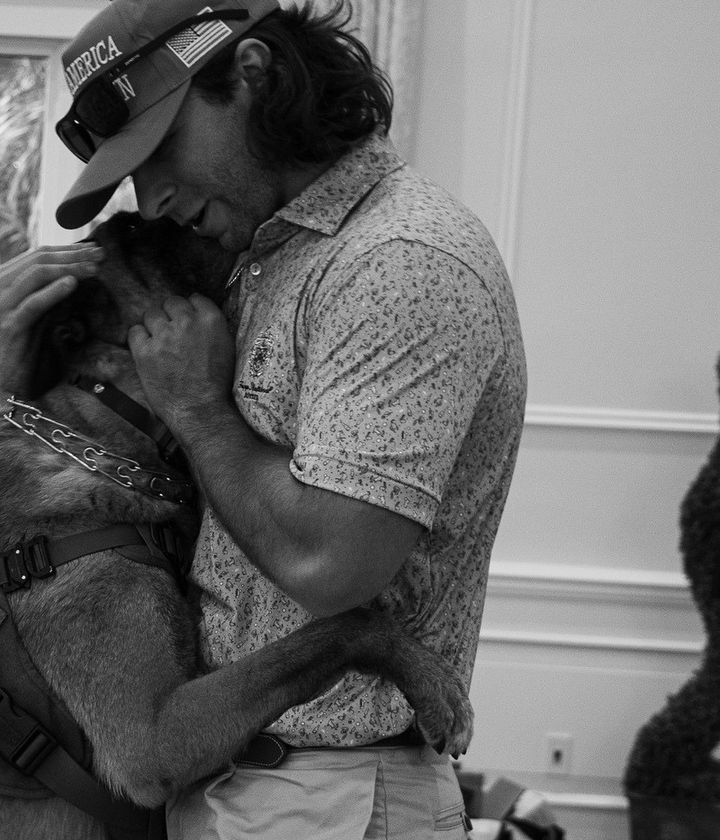 A man in a cap embraces a service dog wearing a Do Not Pet vest